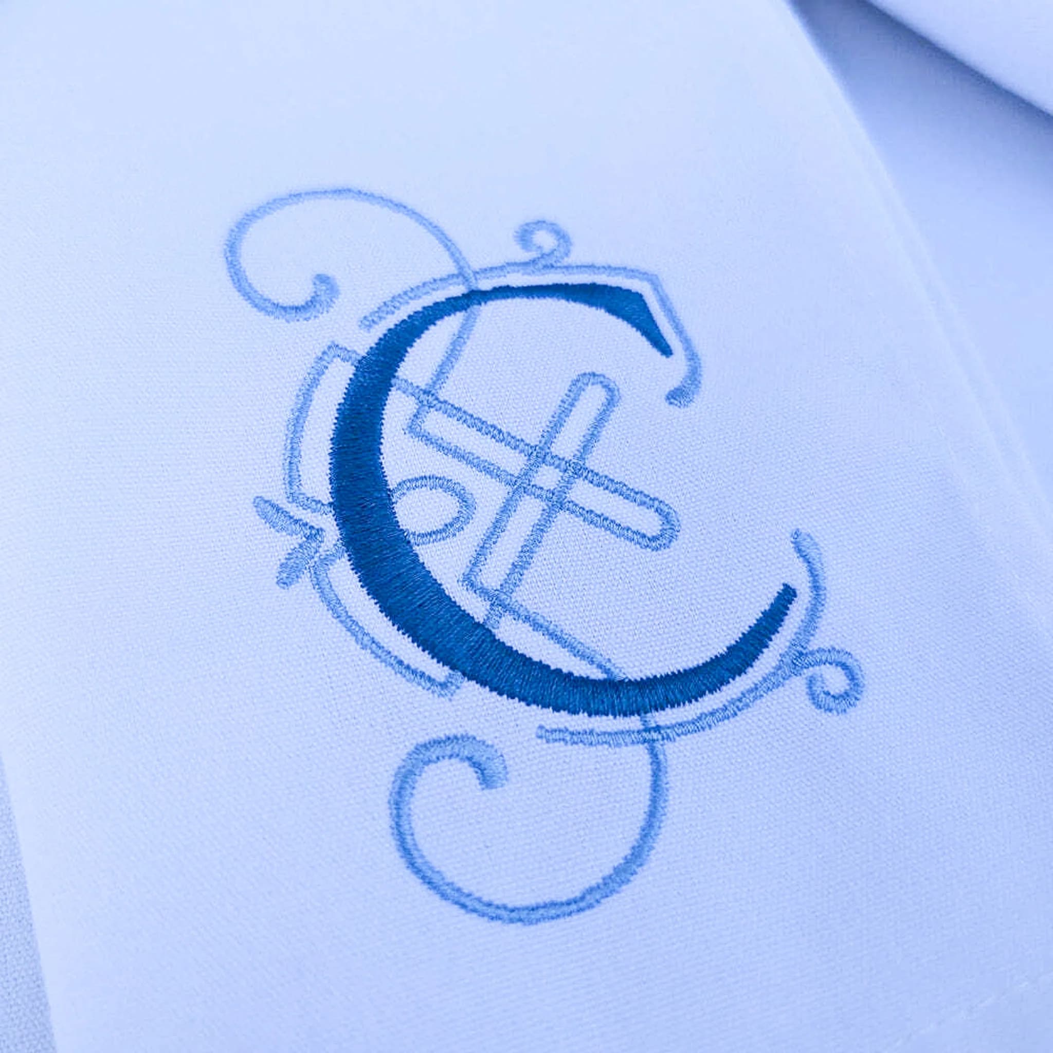 Bold dark blue letter C embroidered over light blue scrollwork on white fabric.